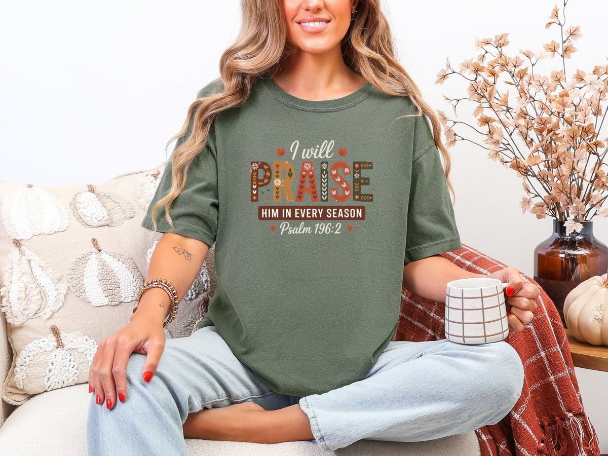 I Will Praise Him in Every Season Christian graphic tee praise in moss color, worn by a woman holding a mug.