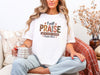 Woman wearing white Christian graphic tee praise reading 'I Will Praise Him in Every Season'.