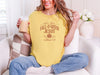 Woman wearing a mustard Are You Foll-o-ween Jesus t-shirt, holding a drink in a cozy setting.