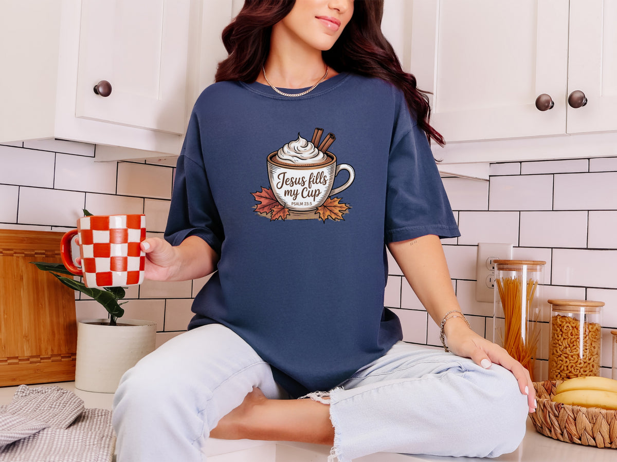 Woman wearing a navy Jesus Fills My Cup t-shirt, holding coffee in a stylish kitchen.