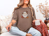 Woman wearing Jesus Fills My Cup t-shirt in espresso, holding a coffee cup next to cozy decor, embodying faith and gratitude.