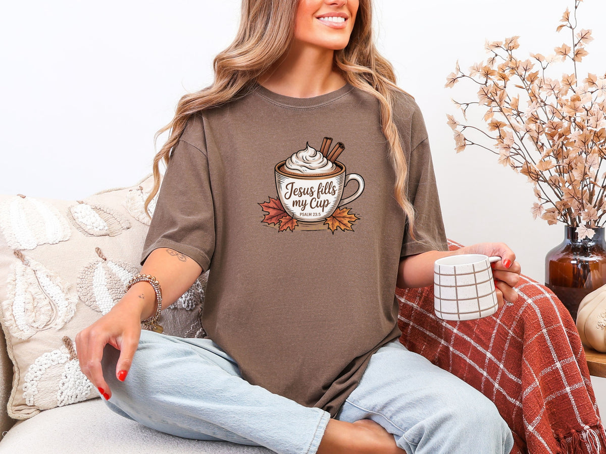 Woman wearing Jesus Fills My Cup t-shirt in espresso, holding a coffee cup next to cozy decor, embodying faith and gratitude.