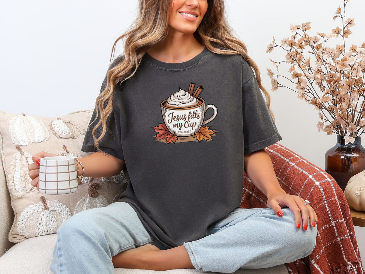 Woman sitting with coffee wearing Jesus Fills My Cup t-shirt in Pepper color, showcasing faith and love.