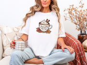 Woman wearing a white Jesus Fills My Cup t-shirt, sipping coffee, surrounded by cozy decor.