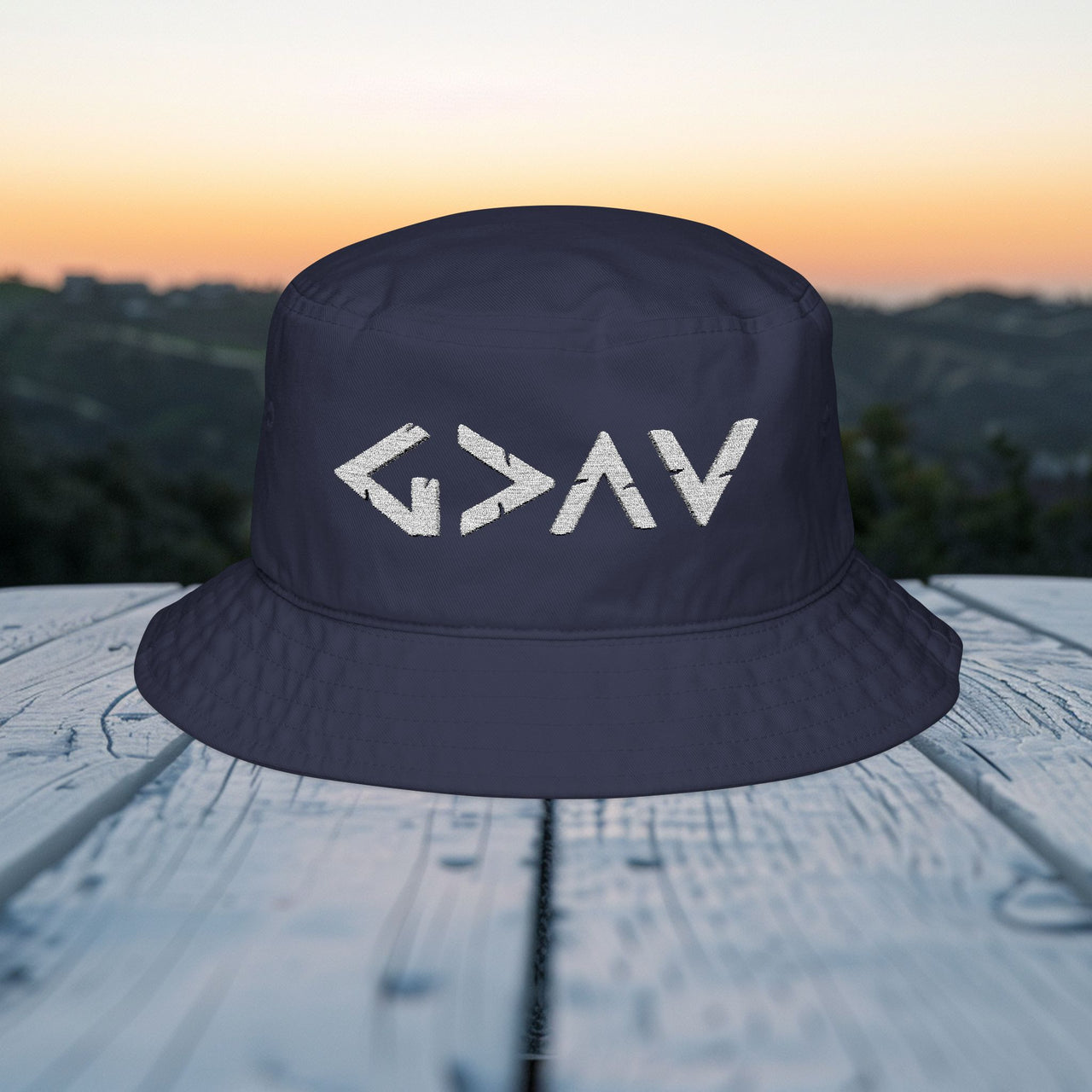 God Is Greater Than Highs and Lows Bucket Hat displayed on a wooden table with a scenic background.