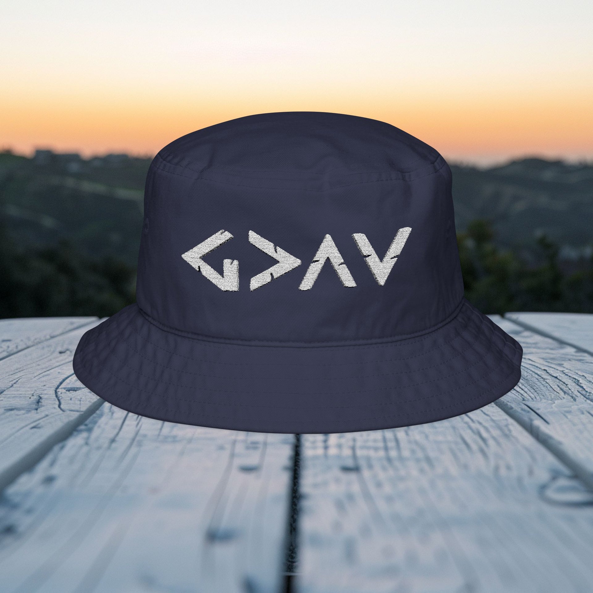 God Is Greater Than Highs and Lows Bucket Hat displayed on a wooden table with a scenic background.