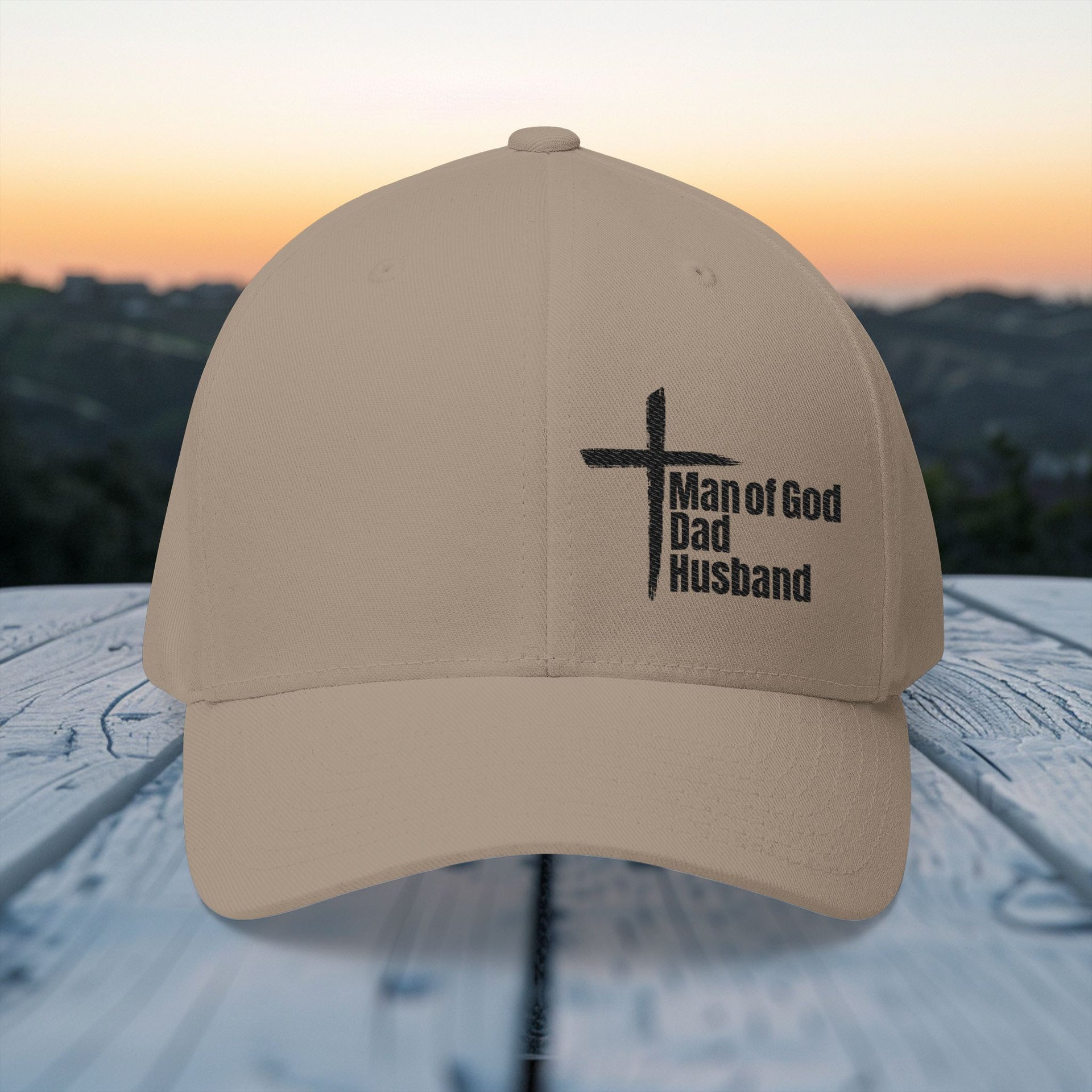 Man of God Dad Husband Embroidered Flexfit Hat in khaki displayed against a sunset background.