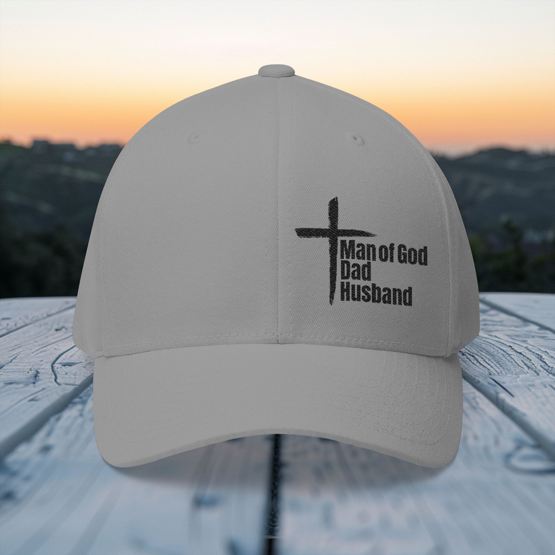 Man of God Dad Husband Embroidered Flexfit Hat in grey displayed outdoors with a cross design.