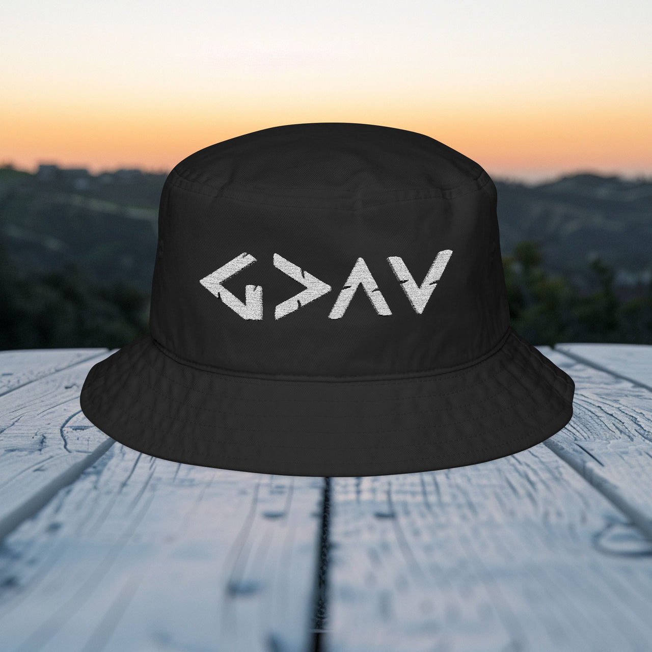 God Is Greater Than Highs and Lows Bucket Hat on a wooden surface with a scenic background.